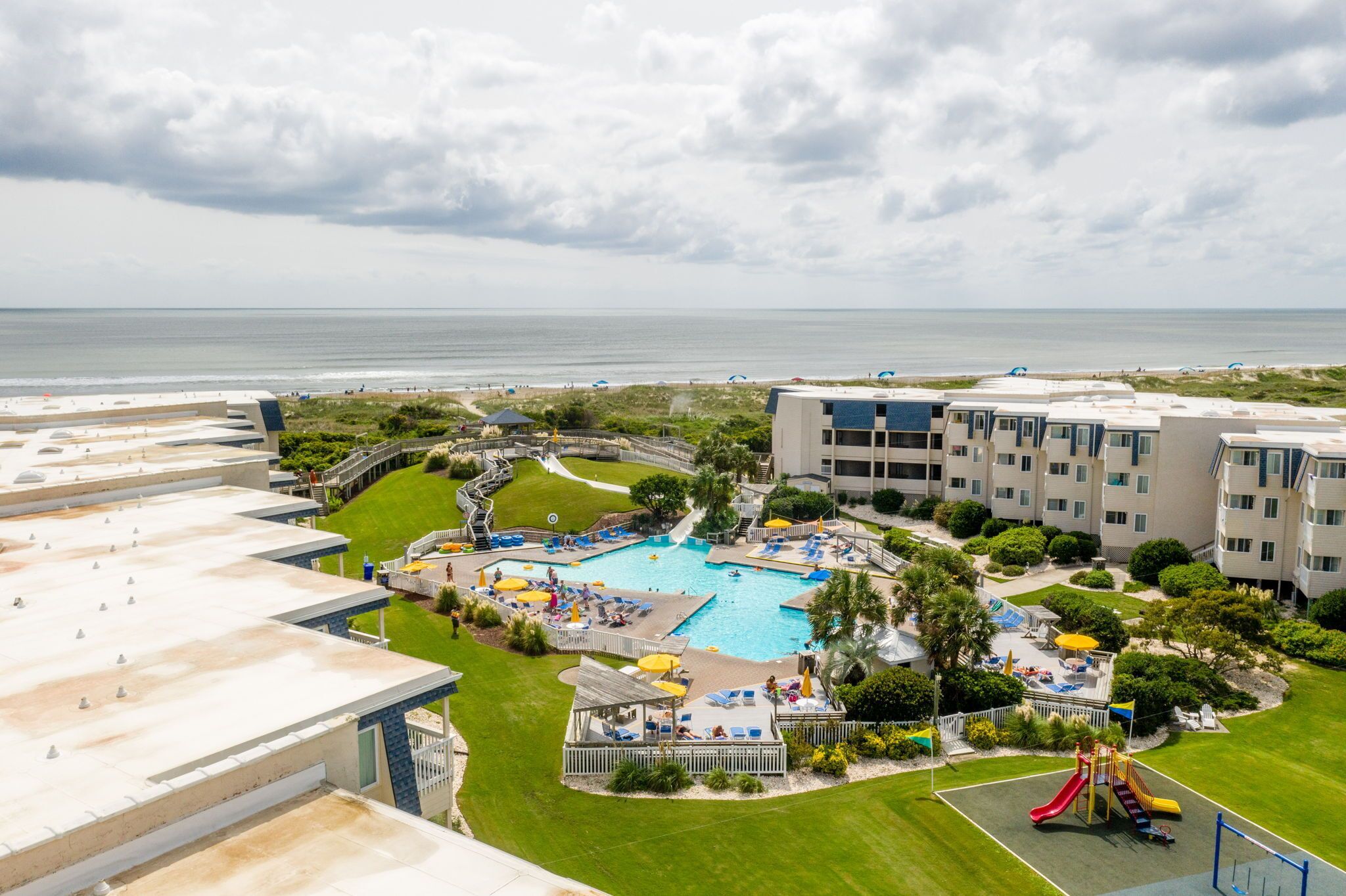 Un resort con piscina centrale, area giochi e vista sulla spiaggia.