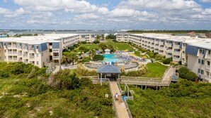 Un resort con varias edificaciones, un área de piscina central y un paseo marítimo que conduce a la piscina.