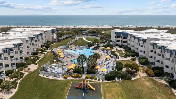 Un edificio residencial de gran altura con una piscina central, rodeado de abundante vegetación y vistas a la playa.