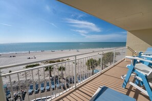 Un balcón con vistas a la playa, que cuenta con una terraza de madera y sillones reclinables azules.