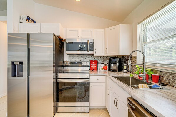 A modern kitchen with stainless steel appliances, white cabinets, and a large window providing natural light. - Quiet Neighborhood! Poolside Oasis in Cape Coral (Cape Coral)