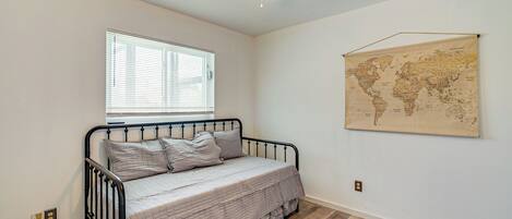 Un dormitorio con una cama individual, ventilador de techo, ventana con persianas y un mapa mundial en la pared.