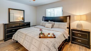 Een slaapkamer met een bed, nachtkastje, dressoir, plafondventilator, raam en een dienblad met een vaas en twee kopjes.