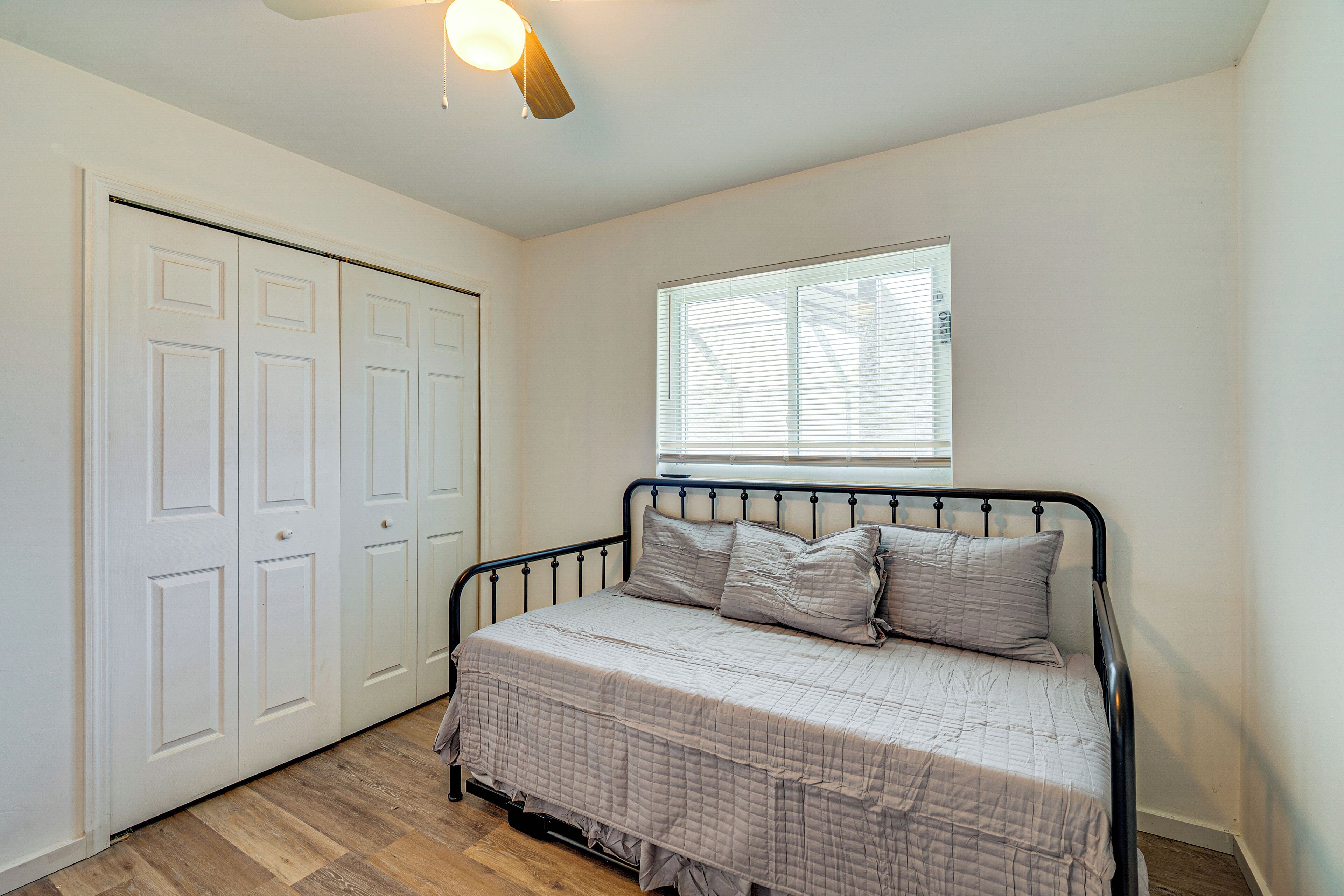 A bedroom with a bed, a window with blinds, a ceiling fan, and a set of white doors.
