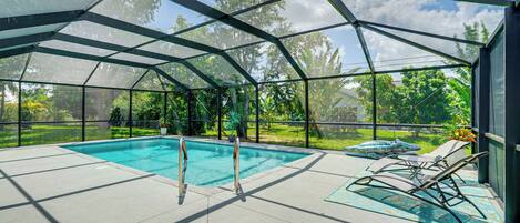 Una piscina cubierta al aire libre con cerramiento de vidrio, rodeada de un patio con sillones y vistas a un jardín exuberante.