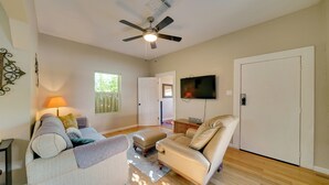 Amplia sala de estar con ventilador de techo, televisor de pantalla plana montado en la pared, sofá de cuero color beige, sofá gris y piso de madera.