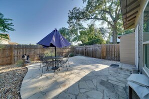 Une terrasse avec un sol en pierre, une table et des chaises, et un parasol violet.