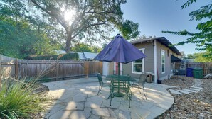 Un patio con suelo de piedra, una mesa y sillas de metal verde, un paraguas morado y una valla de madera.