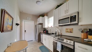 Una cocina con armarios blancos, estufa, microondas y una mesa de comedor con sillas.