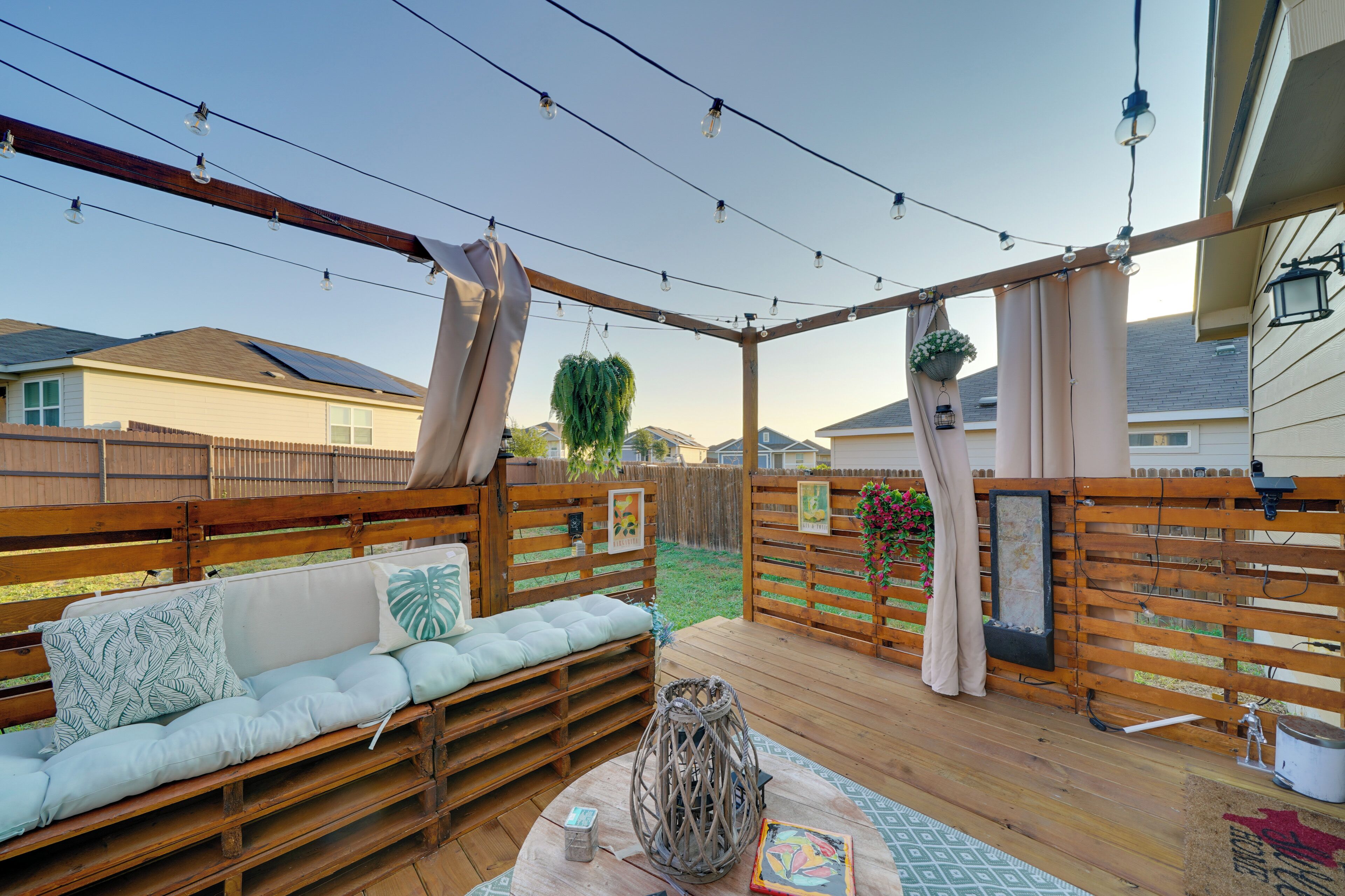 A wooden deck with a sofa, hanging plants, and string lights.