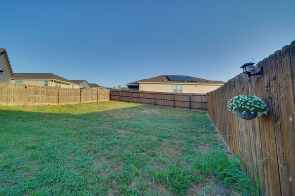 A backyard with a wooden fence, a house with a solar panel, and a hanging flower basket.