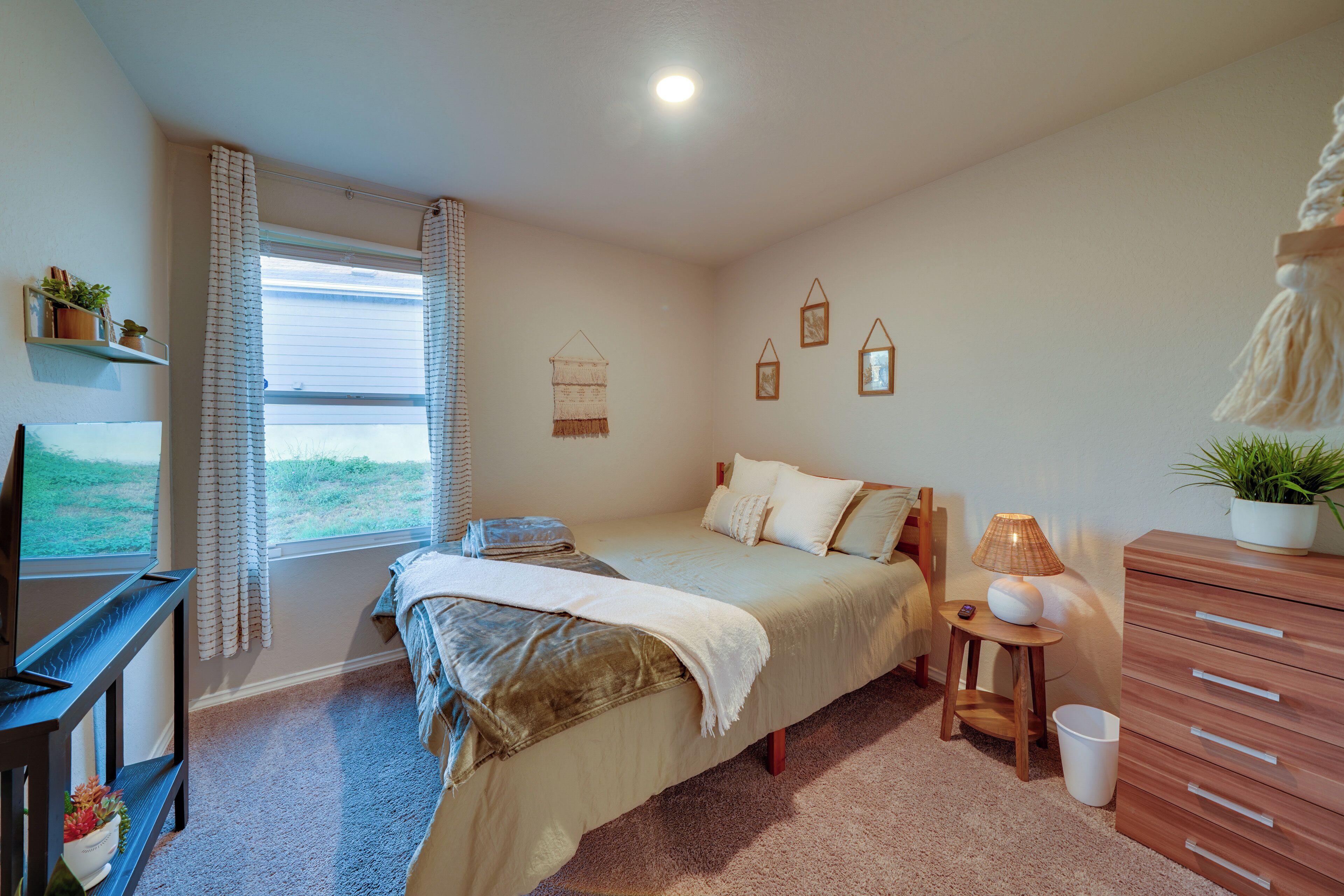A bedroom with a bed, bedside table, lamp, dresser, and window with curtains.