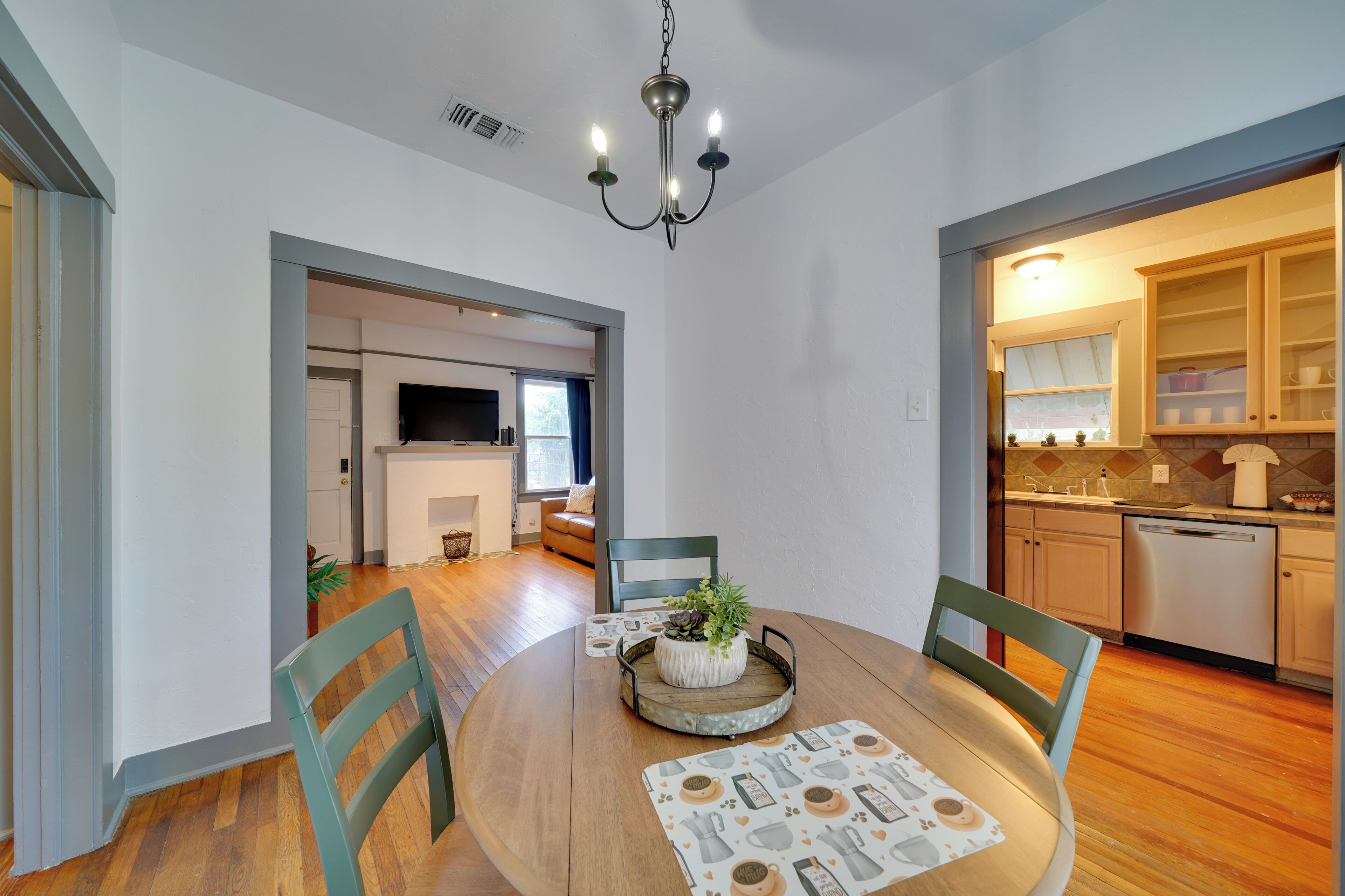 A dining area with a round table, chairs, a chandelier, and a view into the kitchen.