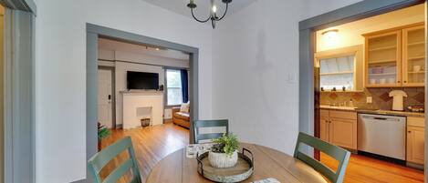 A dining area with a round table, chairs, a chandelier, and a view into the kitchen.