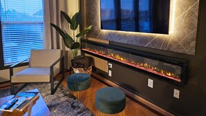Ein modernes Wohnzimmer mit Kamin, einem bequemen Sessel, einer Couch und einem großen an der Wand montierten Fernseher.