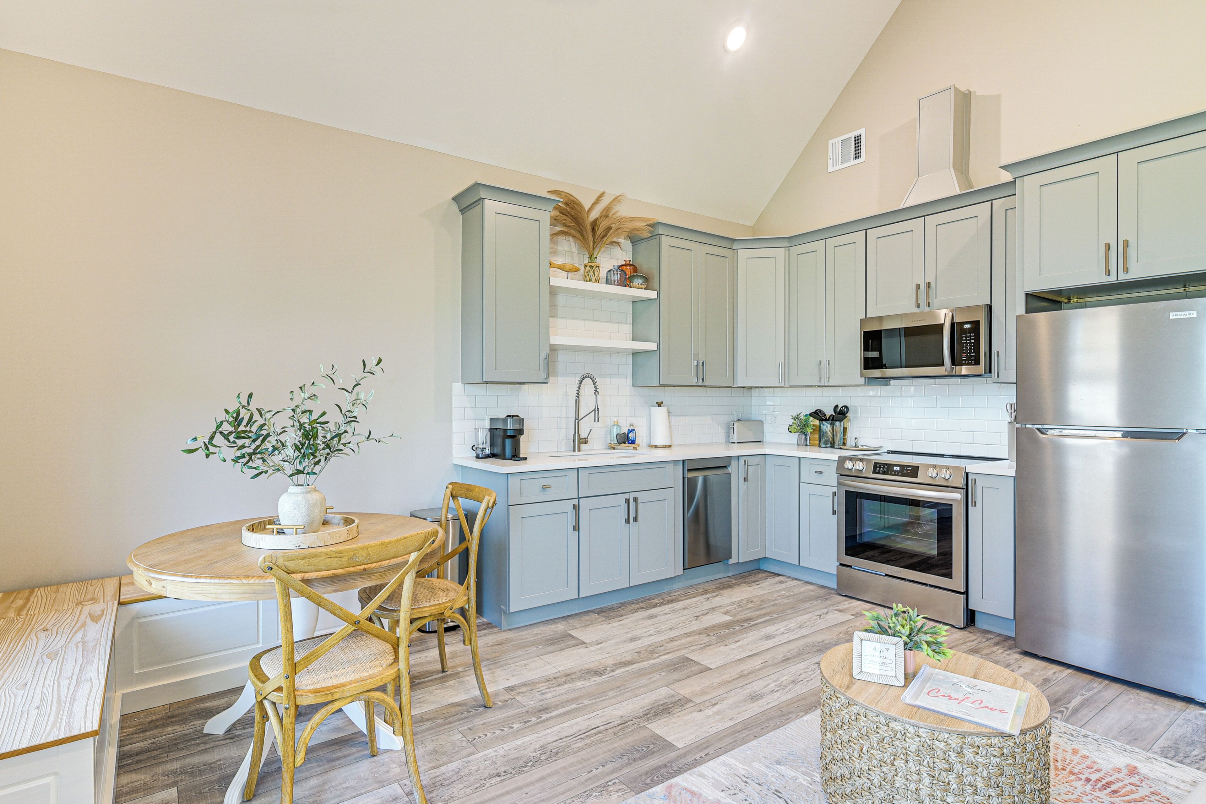 A modern kitchen with light blue cabinets, stainless steel appliances, and a wooden dining table with chairs.