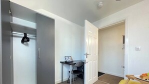 A modern bedroom with a bed, a desk with a chair, and a wardrobe.