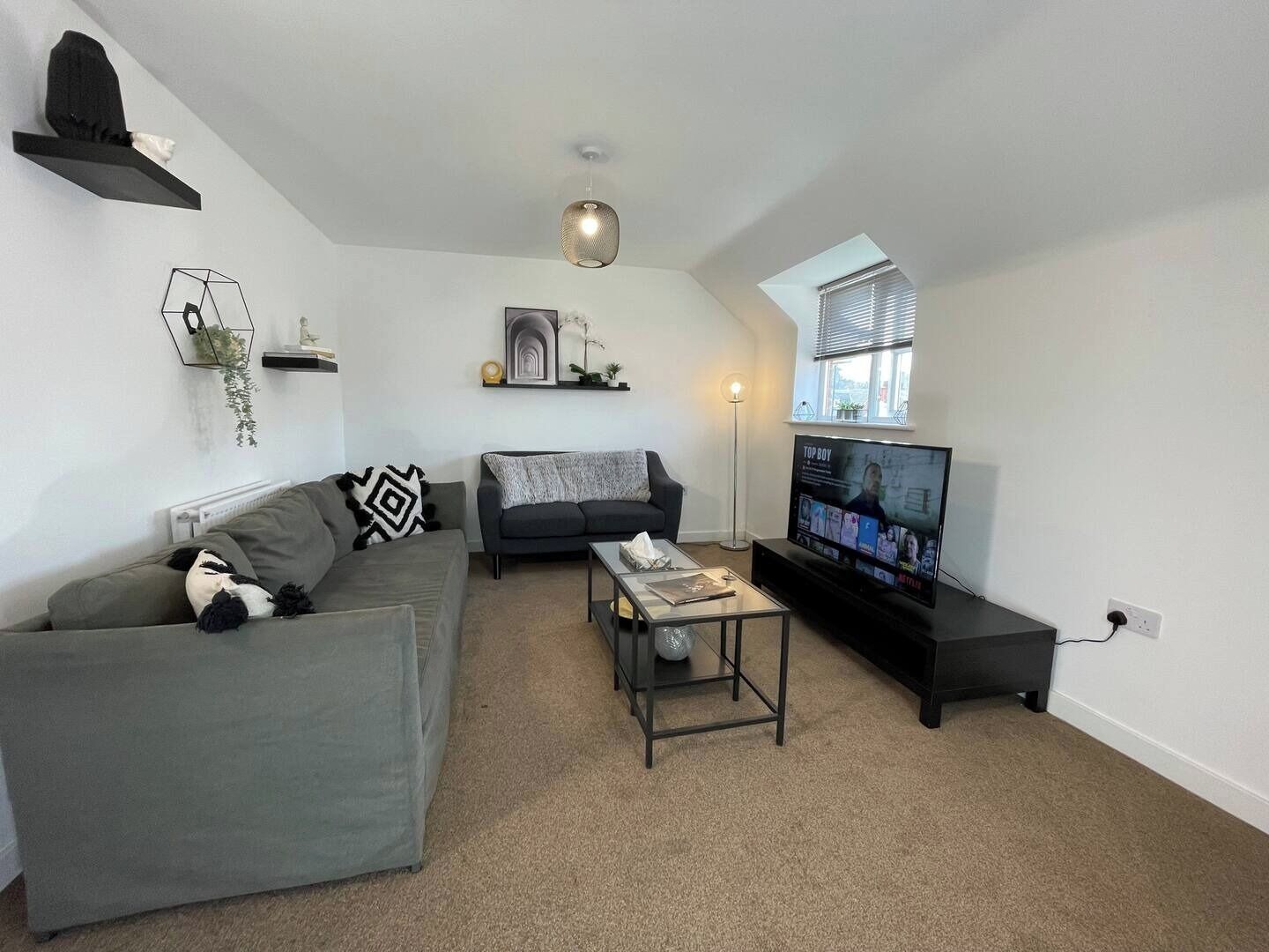 Een moderne woonkamer met een grijze bank, een zwarte fauteuil, een salontafel en een televisie waarop een film wordt afgespeeld.