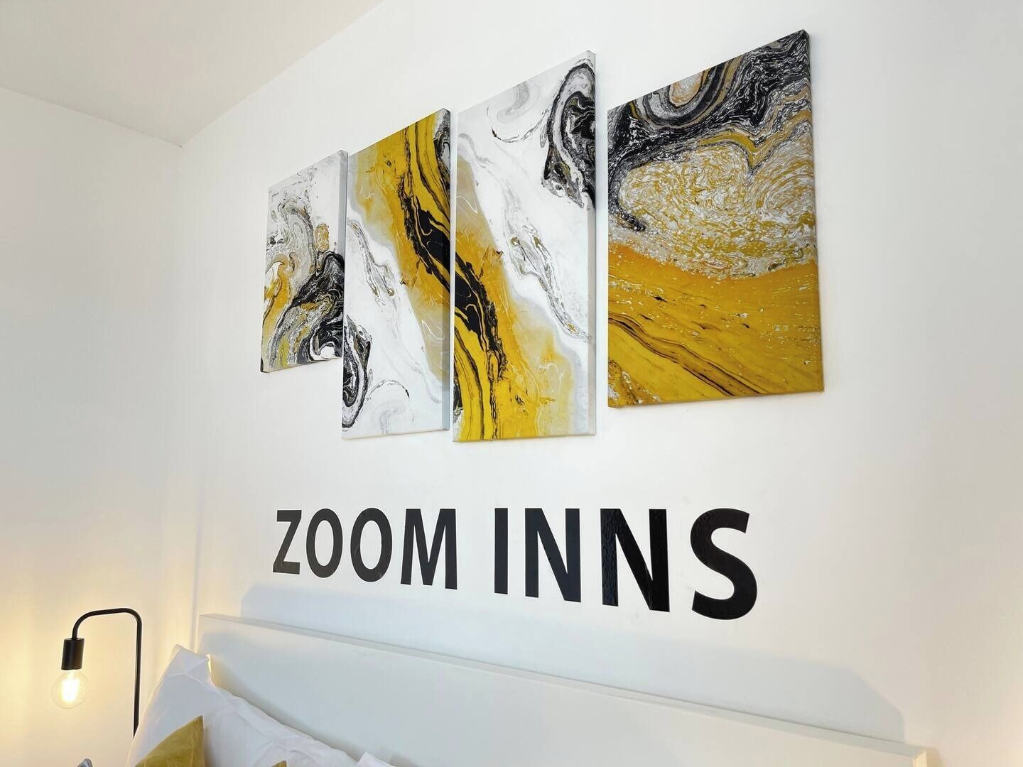 A hotel room with a bed, a bedside table, and three abstract paintings on the wall.