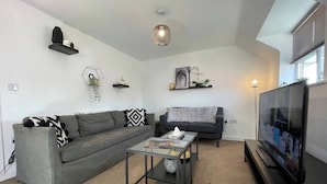 A modern living room with a grey sectional sofa, a coffee table, a flat-screen TV, and decorative items on the walls.