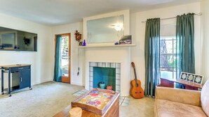 A living room with a fireplace, a sofa, a coffee table, a guitar, and a mirror above the fireplace. - Walk to Mueller Lake Park! Home w/ Patio & Yard (Austin)