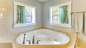 A bathroom with a large bathtub, two windows with curtains, and a towel rack. - Walk to Mueller Lake Park! Home w/ Patio & Yard (Austin)