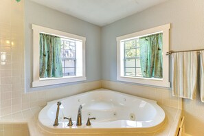 Une salle de bain avec une grande baignoire, deux fenêtres avec des rideaux et un porte-serviettes.