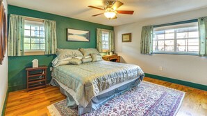 A bedroom with a bed, two windows with curtains, a ceiling fan, and a nightstand with a lamp. - Walk to Mueller Lake Park! Home w/ Patio & Yard (Austin)