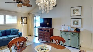 Un salon spacieux avec une table à manger en bois, un canapé bleu, un ventilateur de plafond, un lustre et un téléviseur.