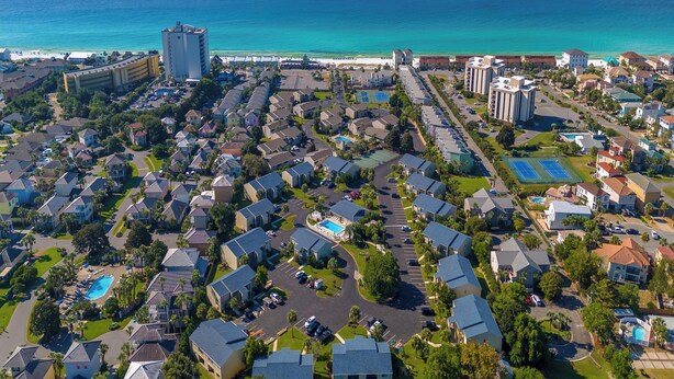 Vue aérienne d’une zone résidentielle côtière, avec des maisons, un grand hôtel et une plage.