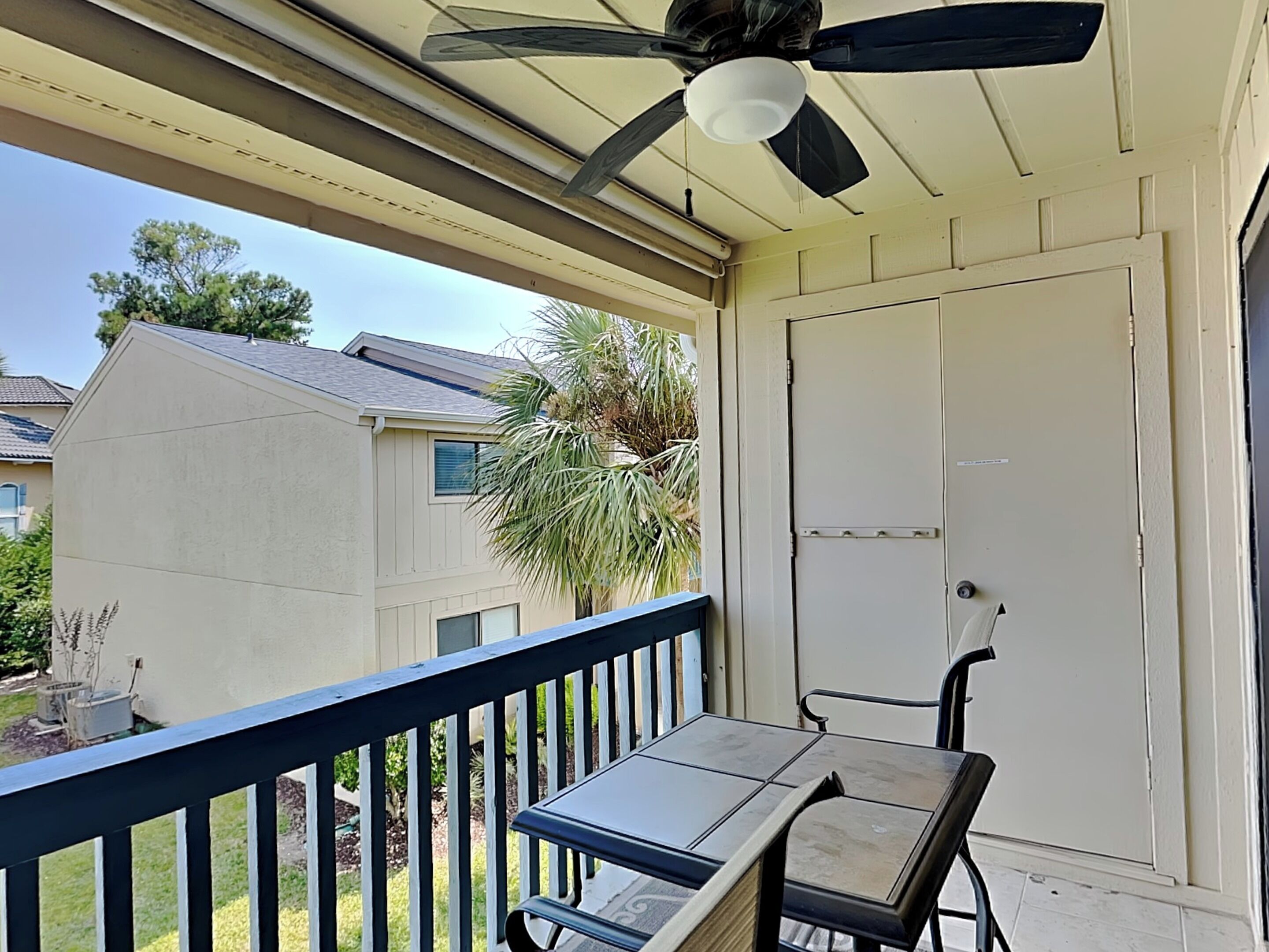 A covered balcony with a table and chairs, a ceiling fan, and a door.