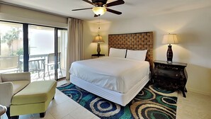 Une chambre d’hôtel avec un grand lit, un ventilateur de plafond, une table de chevet avec une lampe, une chaise et une vue sur l’extérieur.