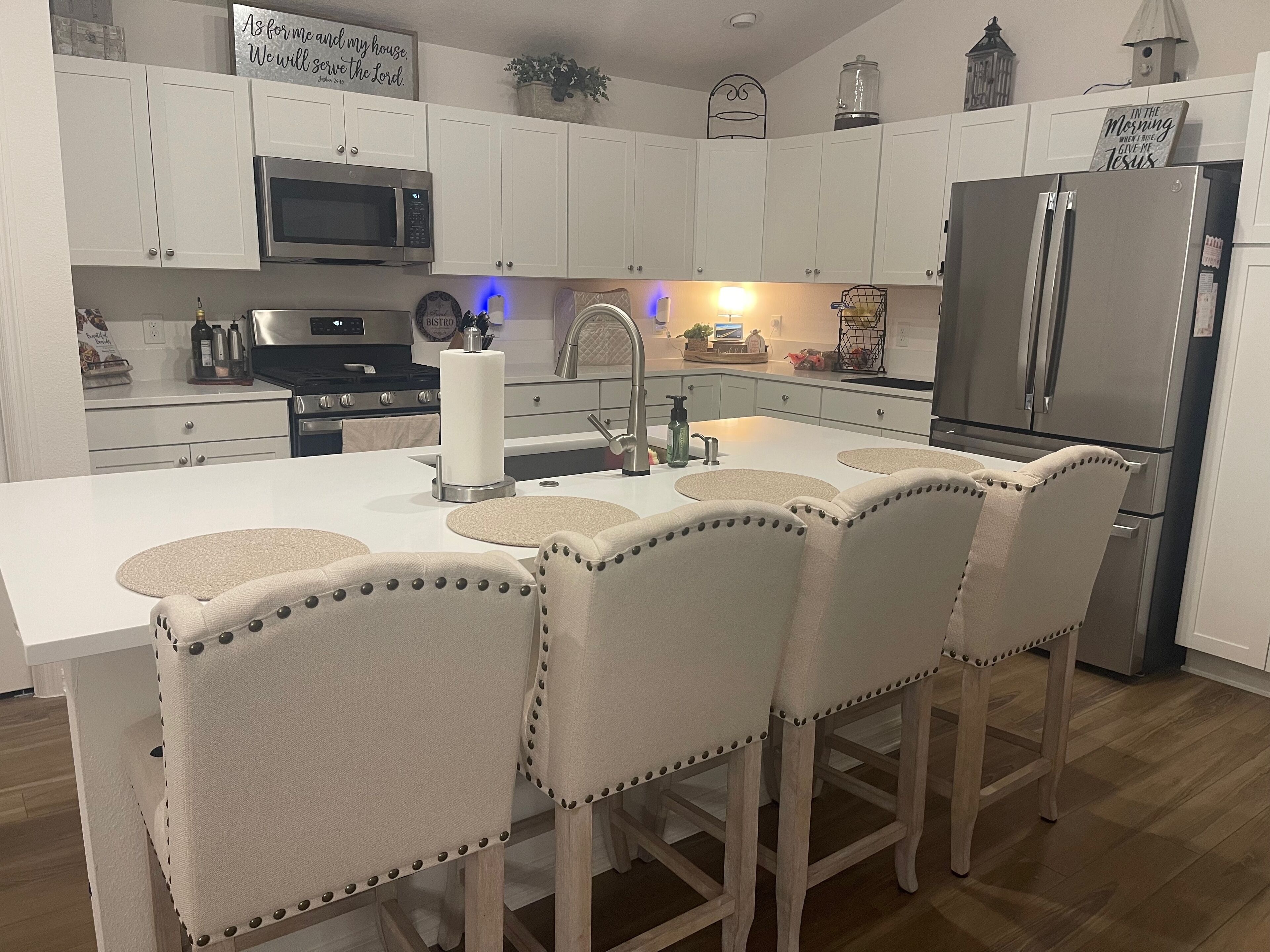 A modern kitchen with white cabinetry, a central island with bar stools, a stainless steel refrigerator, and a microwave above the stove.