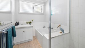 Een moderne badkamer met een douchecabine van glas, een witte badkuip en een wastafel met spiegel.