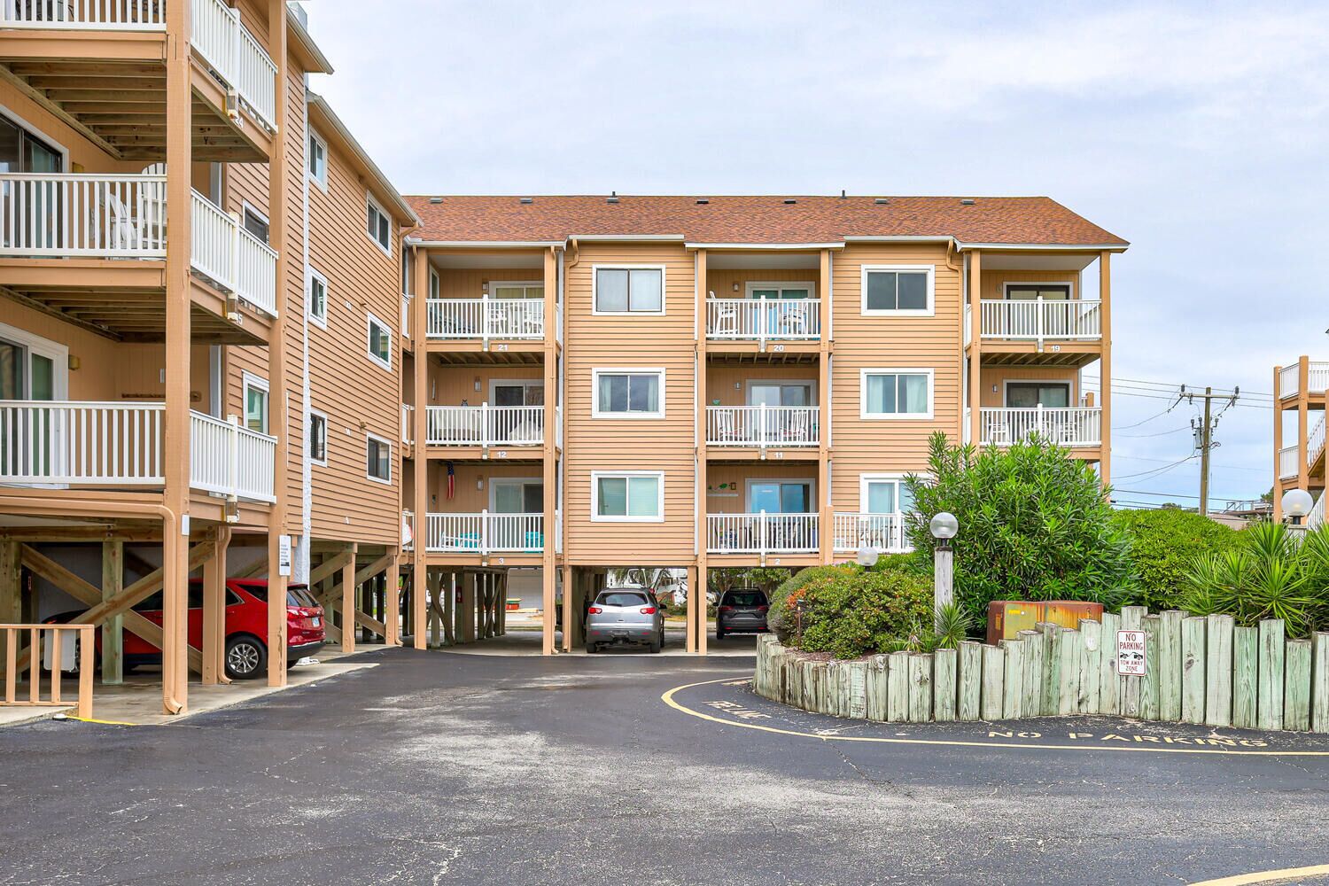 A multi-story apartment building with balconies, a parking area, and a 'No Parking' sign.