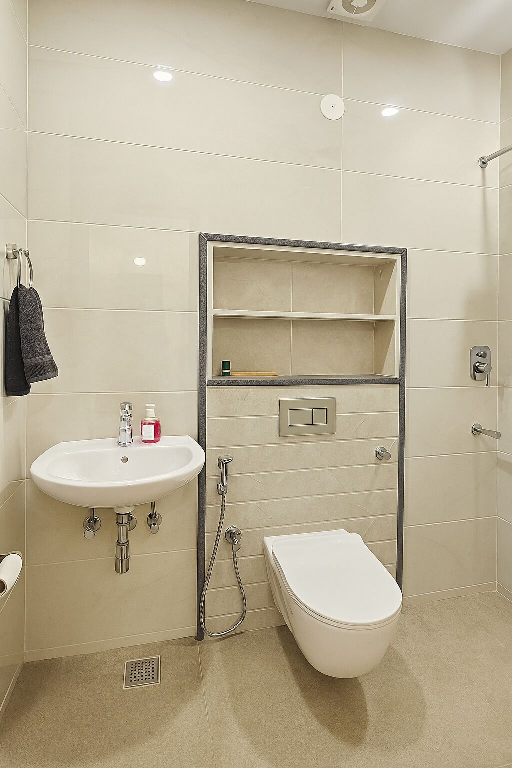 Une salle de bain avec un lavabo, des toilettes et une douche, tous de couleur blanche. On y trouve un porte-serviettes sur lequel est suspendue une serviette, ainsi qu’une étagère au-dessus du lavabo.