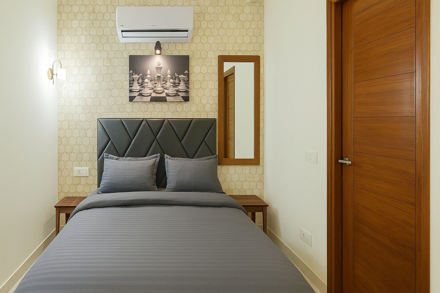 A bedroom with a bed, a headboard, a nightstand, a wall-mounted air conditioner, a wall-mounted light, a framed picture, a mirror, and a wooden door.