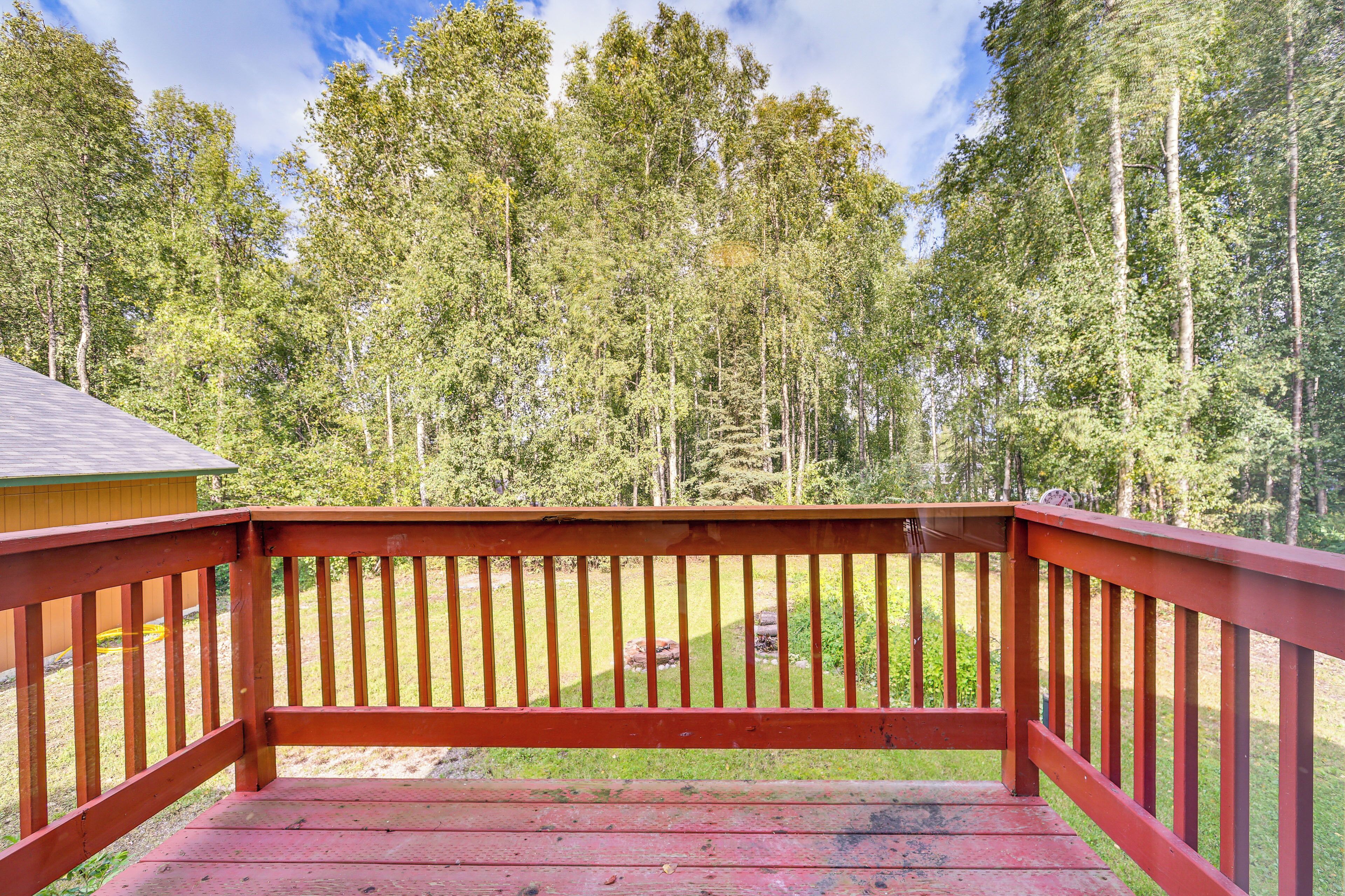 A wooden deck with a railing, overlooking a forested area with tall trees.