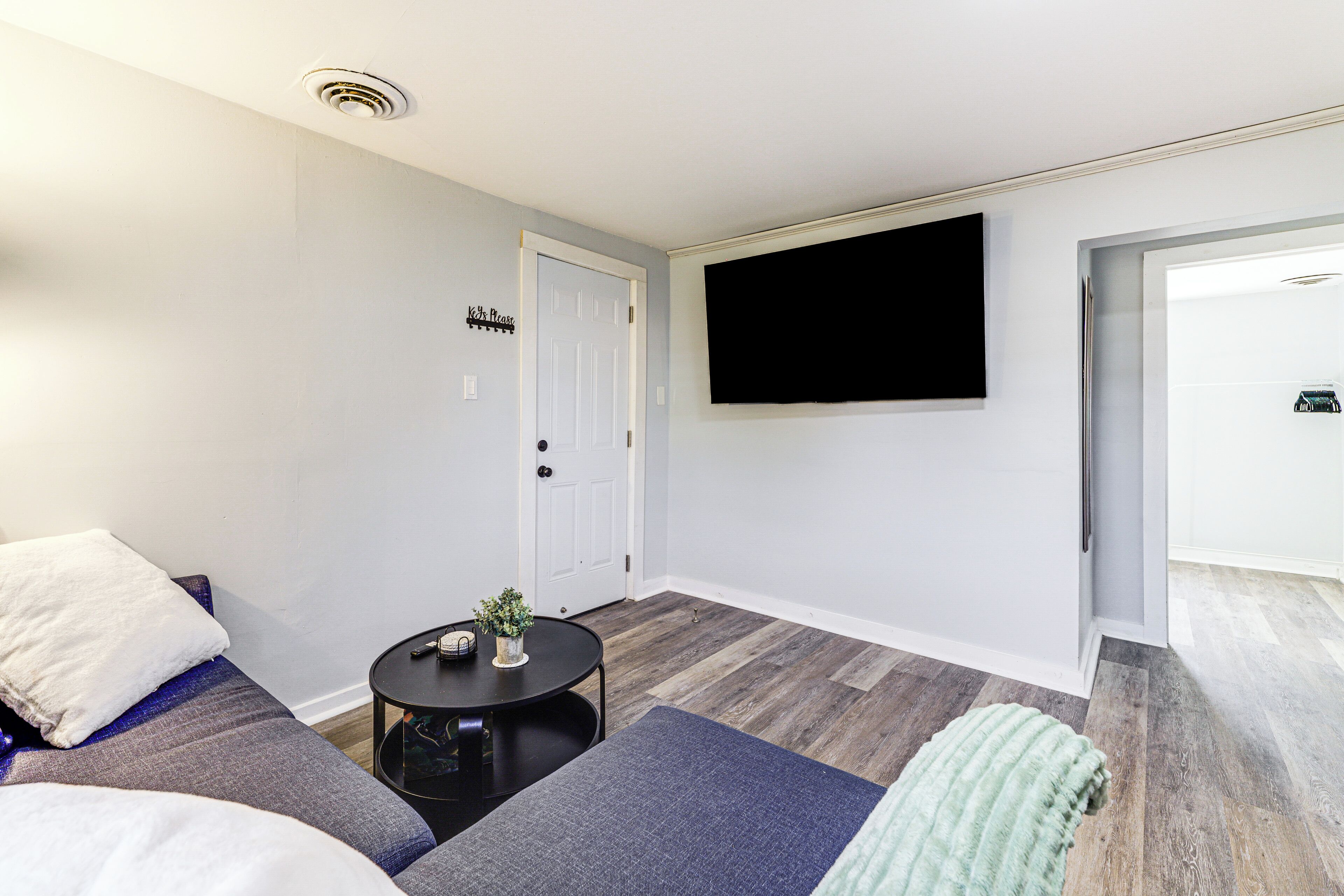 A modern living room with a sofa, a small round table, and a flat-screen TV mounted on the wall.