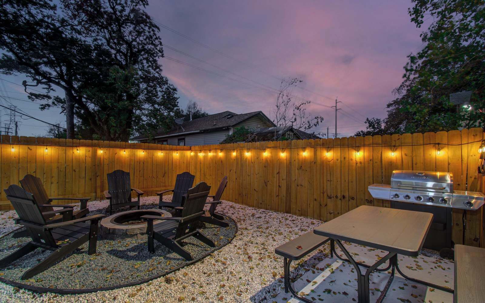 Ein Garten mit Holzzaun, Gartenmöbeln, Grill und Lichterkette.