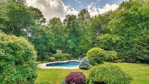 A backyard with a swimming pool, surrounded by lush greenery and various shrubs.