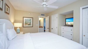 Ein Hotelzimmer mit einem großen Bett, einem Deckenventilator, einem Fernseher und Blick auf den Strand durch eine geöffnete Tür.