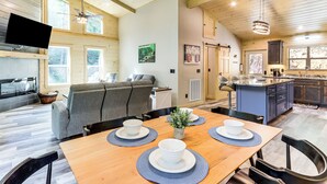 Amplia sala de estar con una mesa de comedor de madera dispuesta para cuatro personas, un sofá gris y una cocina con una isla azul.