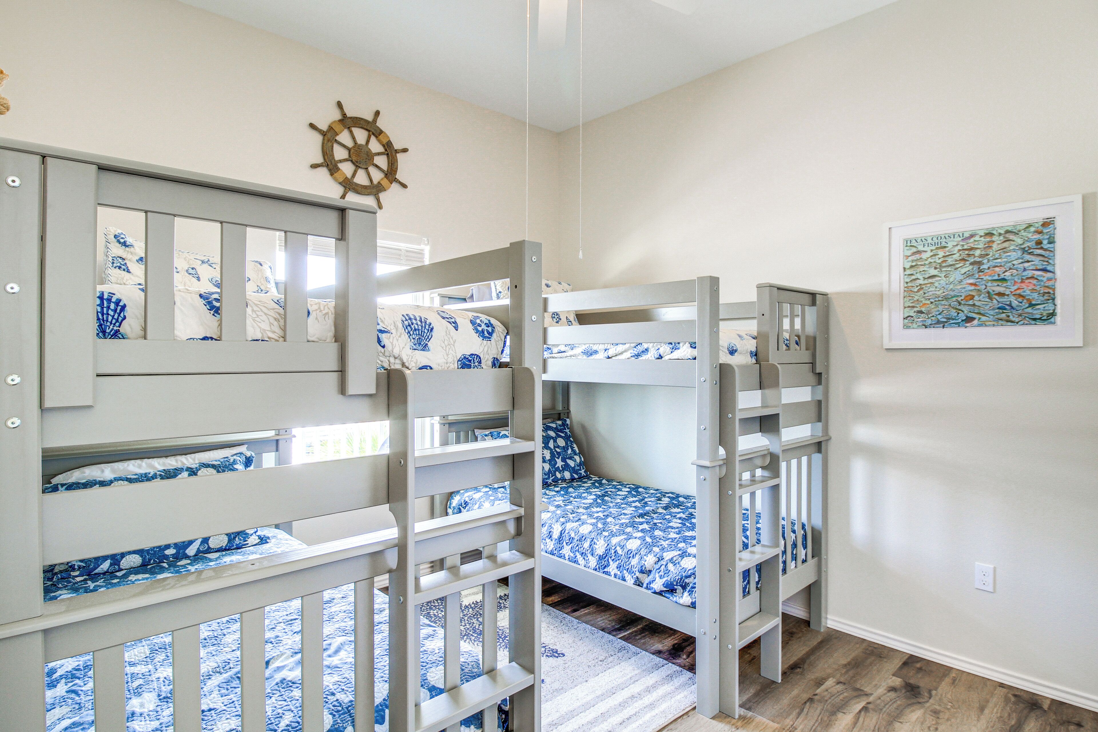 Een slaapkamer met stapelbed, een decoratie van een scheepswiel, een ingelijste afbeelding van vissen en een houten vloer.