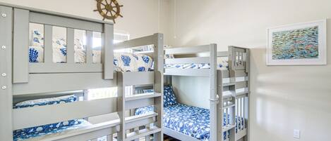 Een slaapkamer met stapelbed, een decoratie van een scheepswiel, een ingelijste afbeelding van vissen en een houten vloer.