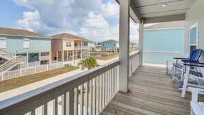 A wooden deck with white railings, a covered area with chairs, and a view of colorful houses. - Home w/ Pool Access in Rockport! (Rockport)