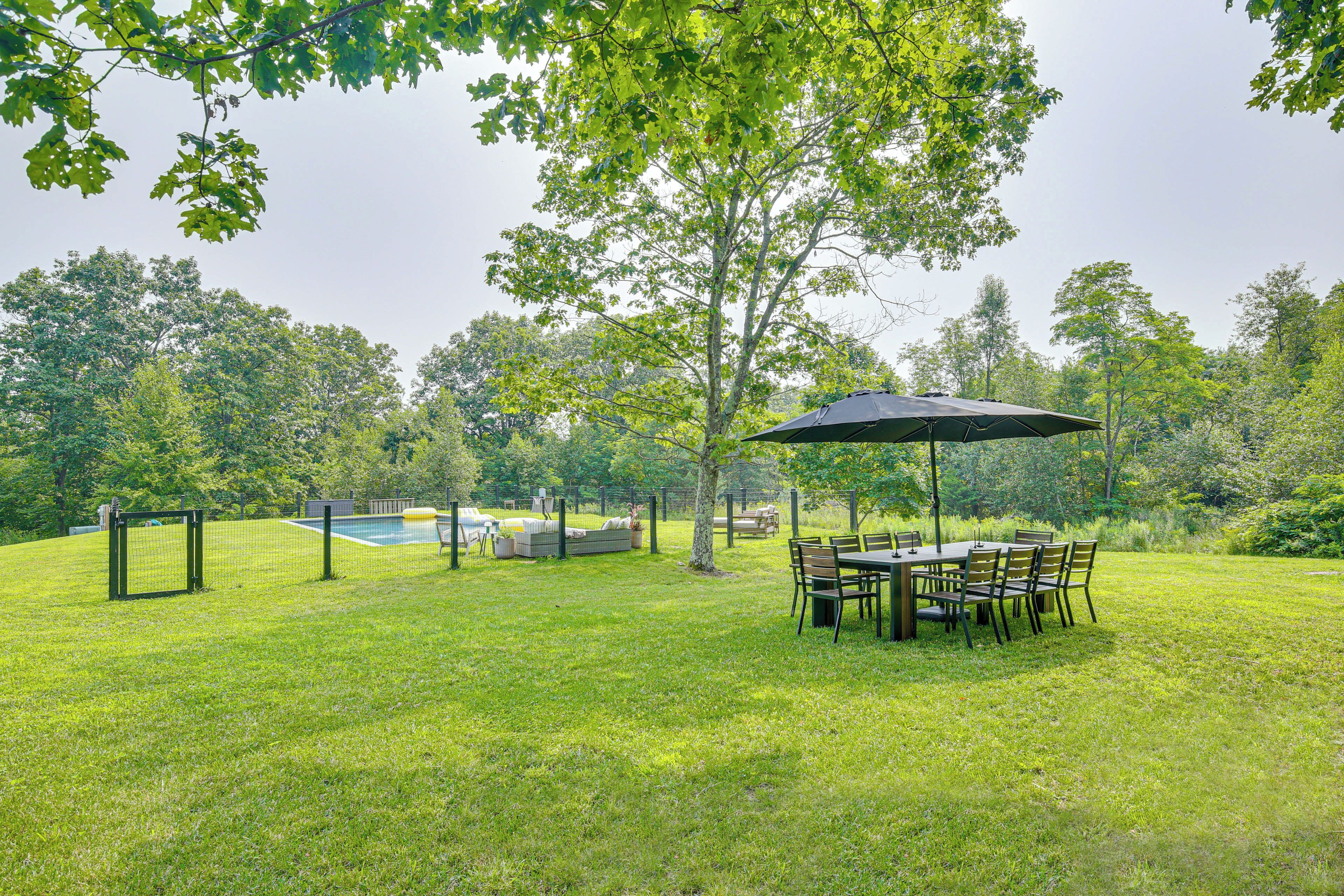 A grassy outdoor area with a table and chairs under a canopy, surrounded by trees.