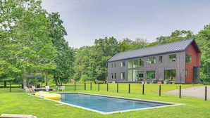 Een modern huis met een zwembad, omgeven door een verzorgd gazon en bomen.