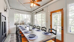 A dining area with a long wooden table set for six, surrounded by chairs, large windows, and a ceiling fan. - Dock + Views: Scenic Group Retreat on Grand Lake! (Eucha)