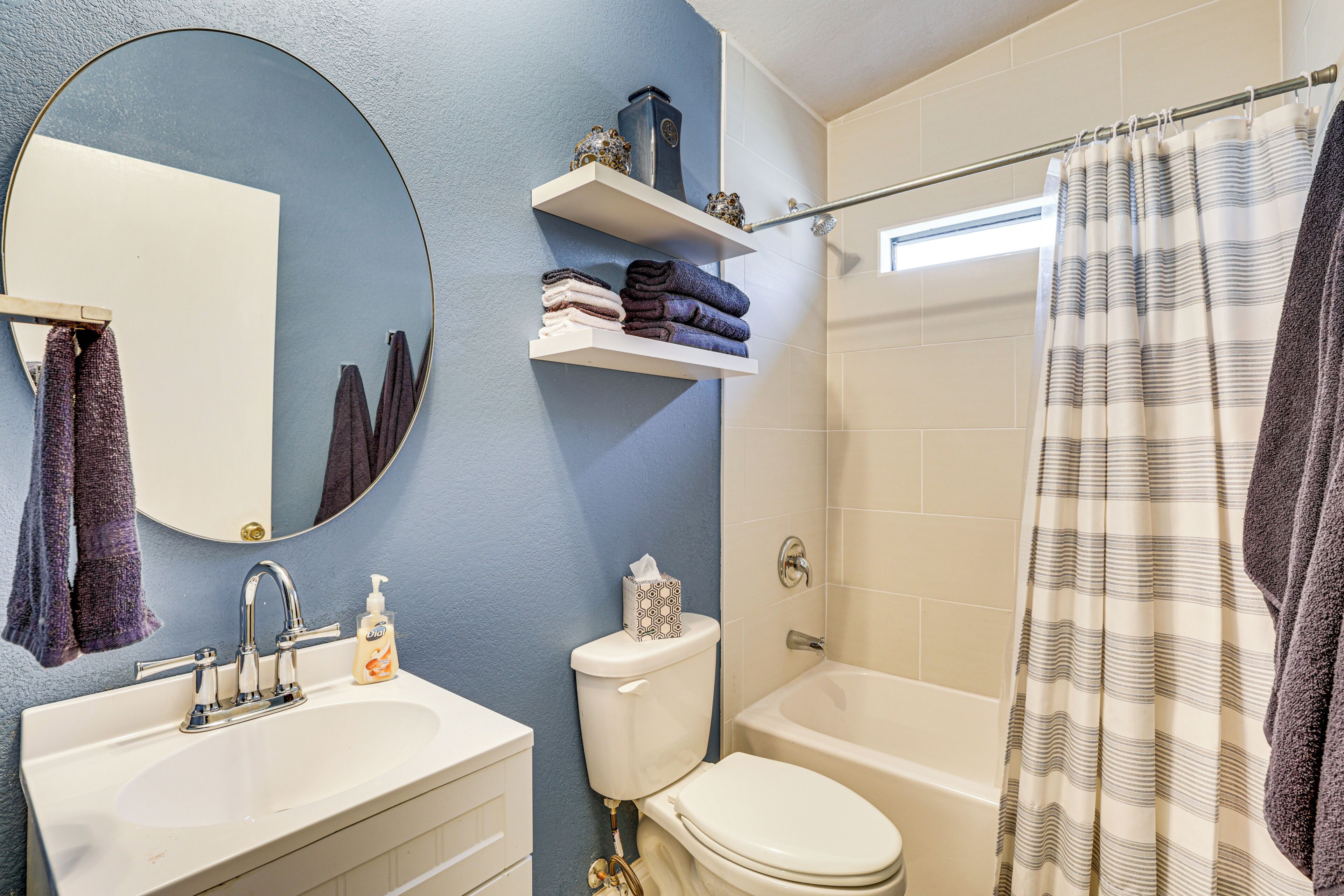 A bathroom with a sink, toilet, and bathtub. There are shelves above the toilet with towels and toiletries.